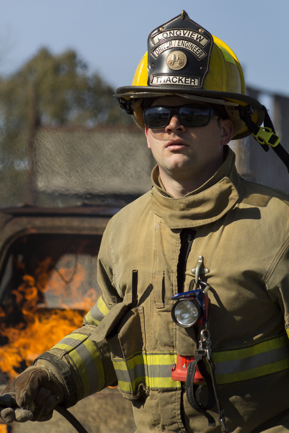 Fire Academy student training at the drill field with a car fire behind him