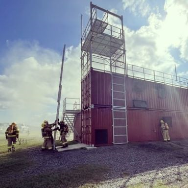 Fire academy students in bunker gear leaning a 30 foot ladder on the burn building