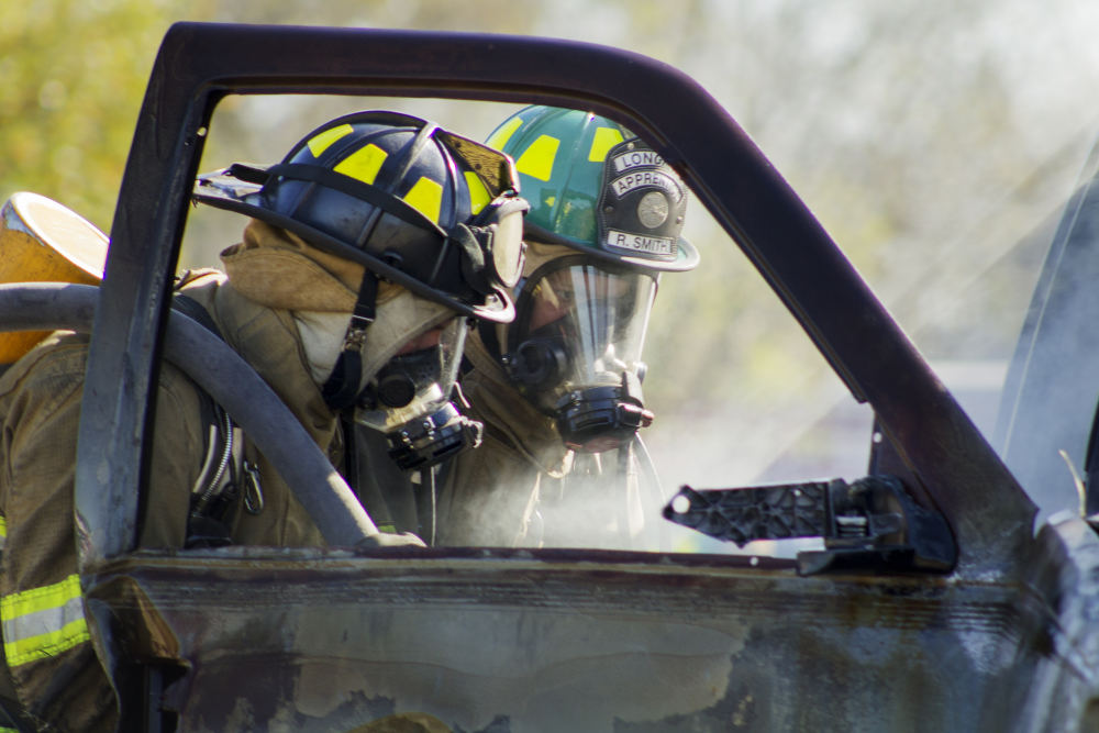 Two fire academy students putting out a car fire with the car door open